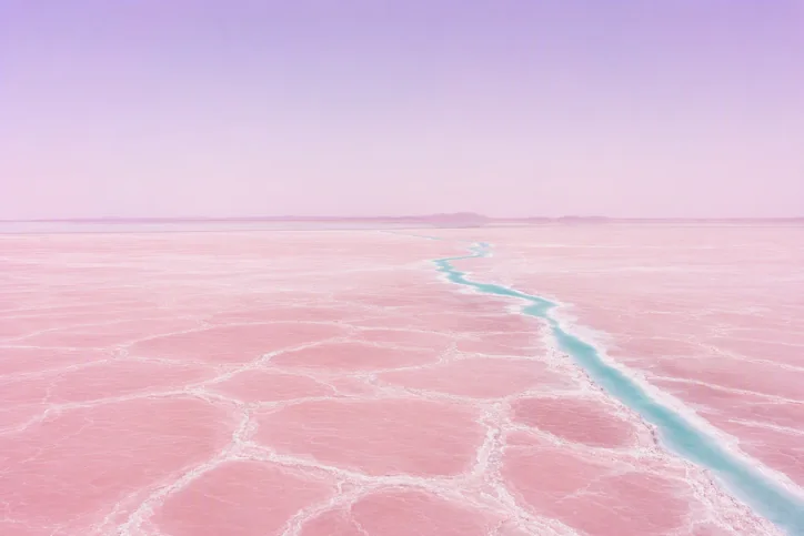Pink salt flats beneath a vast pastel sky. Minimalist high-key aerial landscape photography in pale pink and lilac.